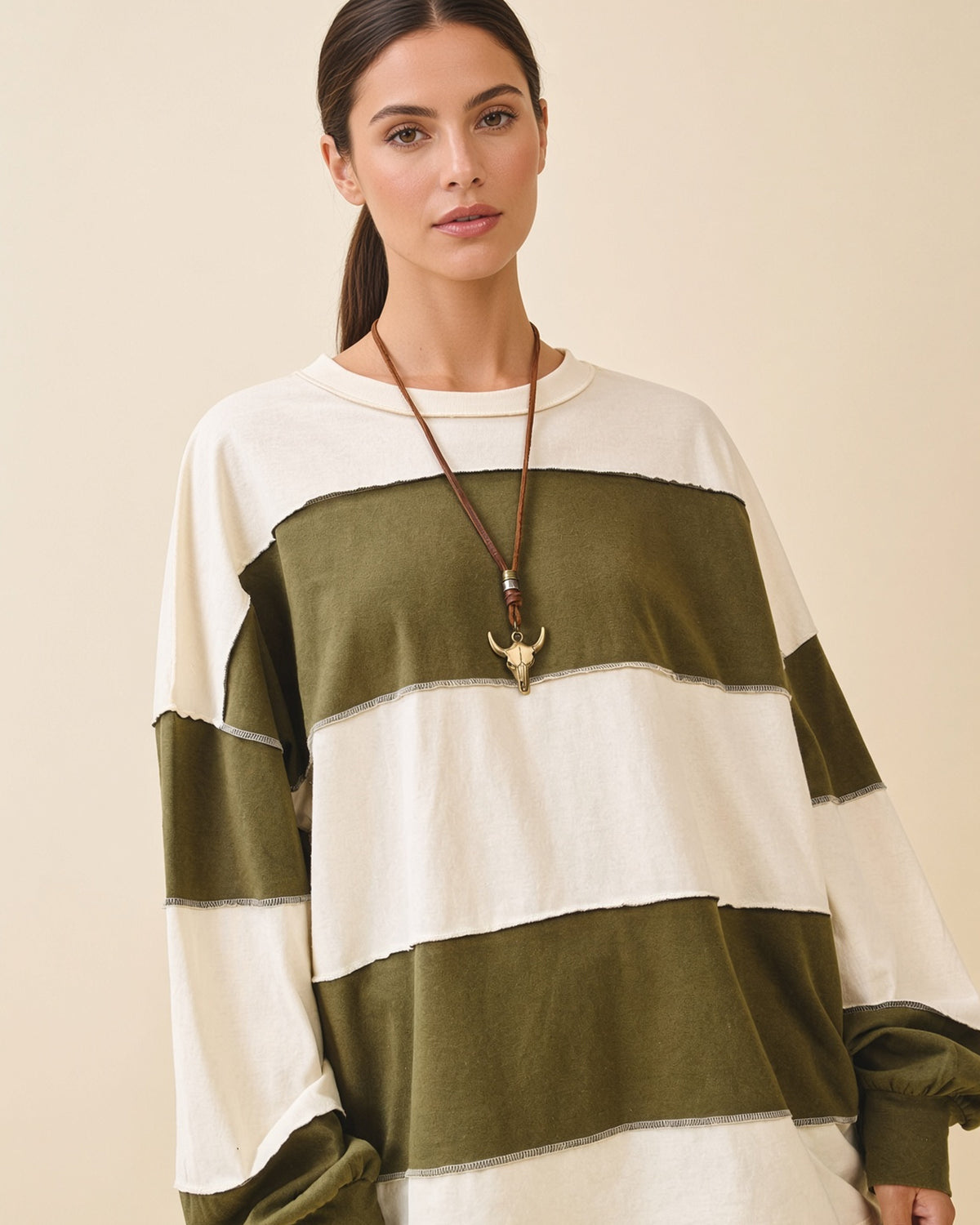 Model wearing a relaxed fit long sleeve top with crew neck, wide olive and butter color blocks and exposed seams.