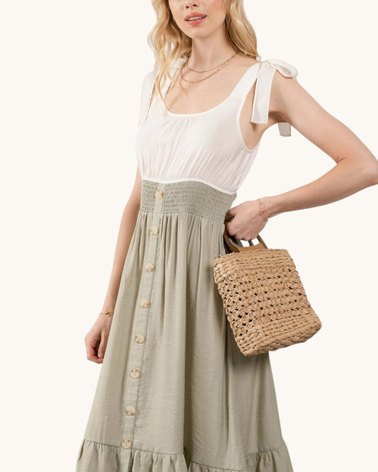 Woman wearing a white top and green skirt holding a woven bag on a white background.