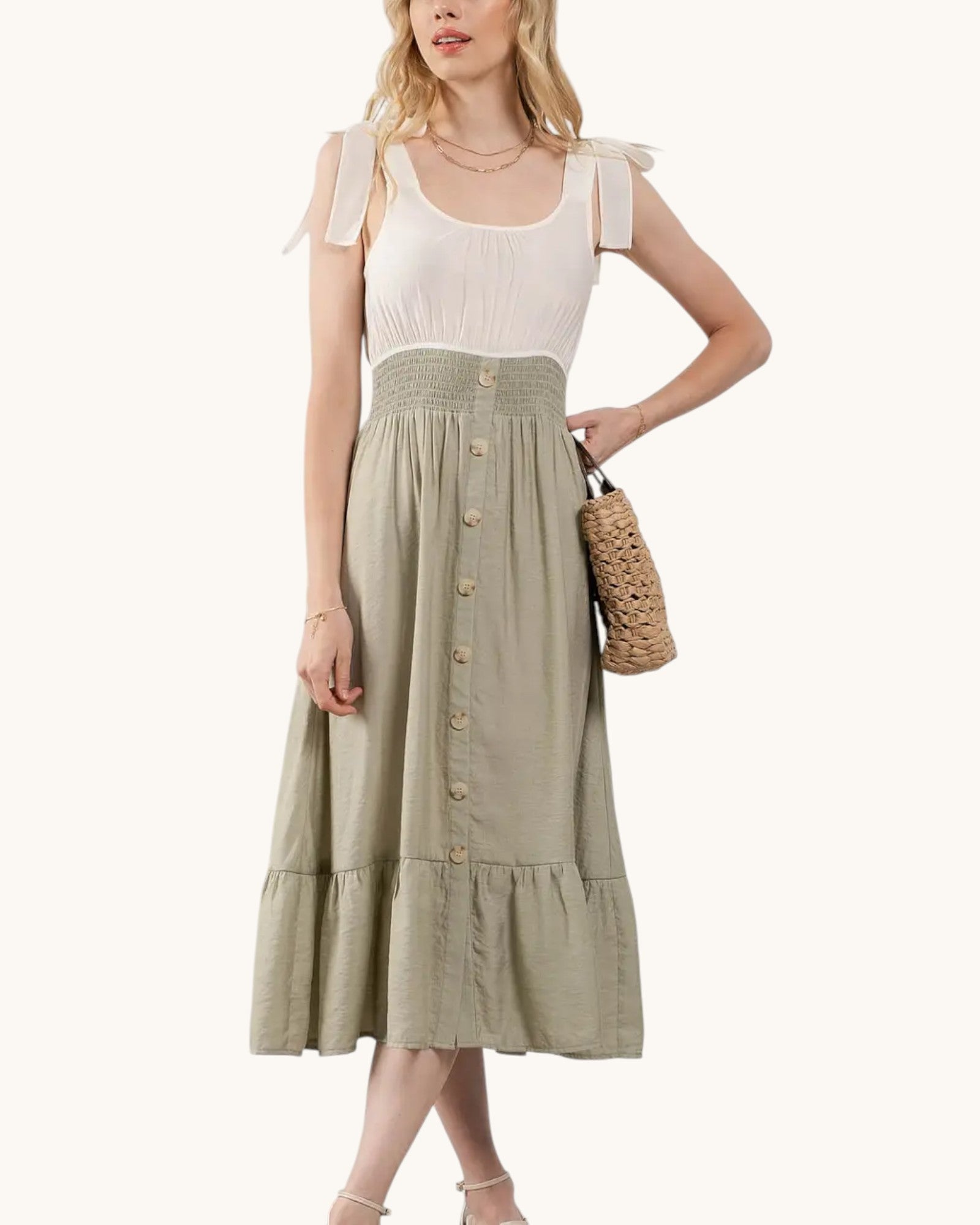 Woman wearing a sleeveless midi dress with a cream top contrasting against a sage green skirt with buttons on a white background.