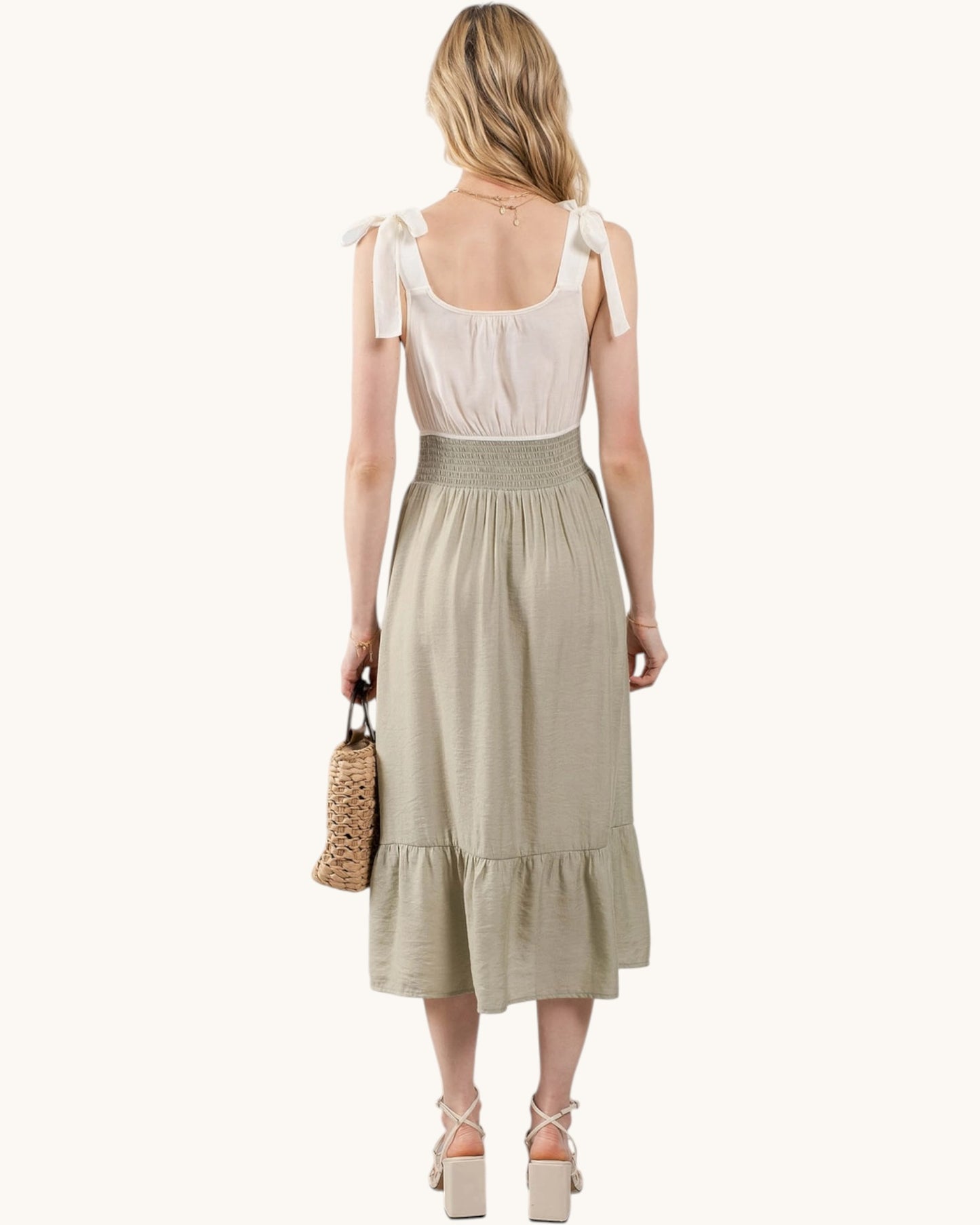 Back view of a woman wearing a sleeveless midi dress with a cream top contrasting against a sage green skirt.