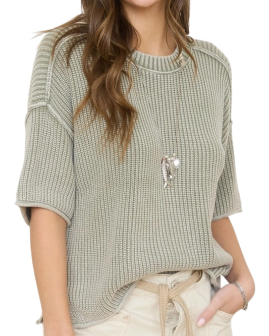 Woman wearing a light green washed short sleeve knit sweater on a white background.