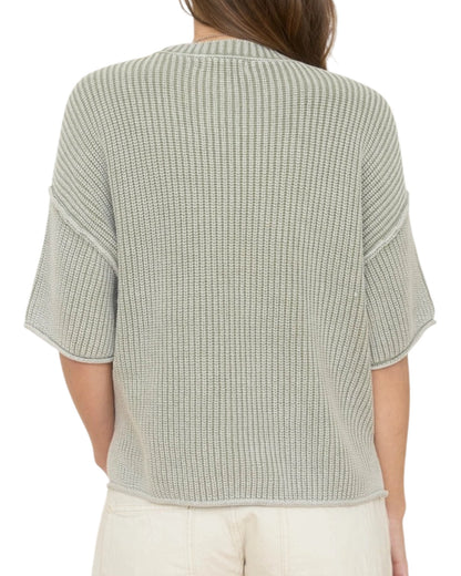 Woman wearing a light green washed short sleeve knit sweater on a white background.