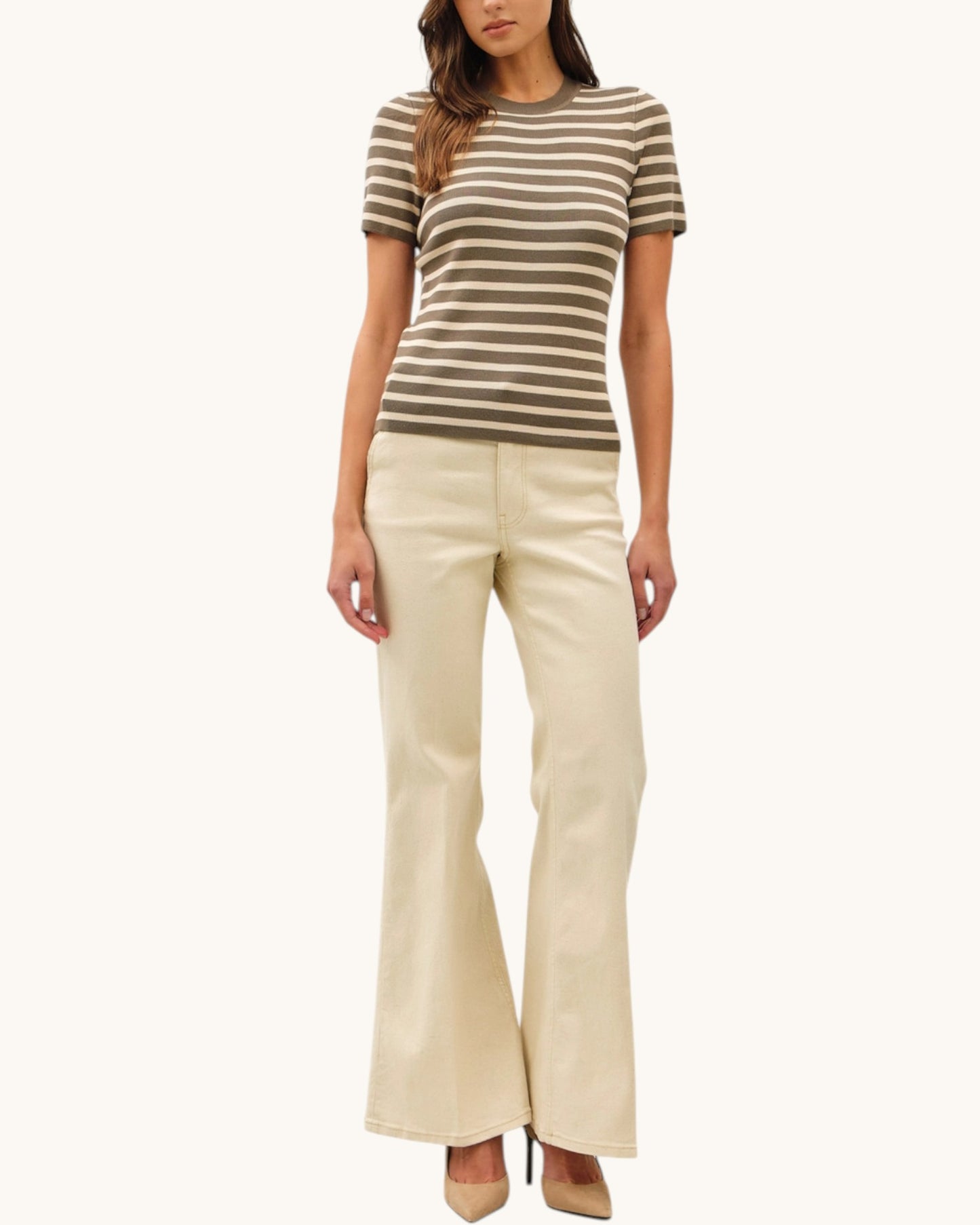 Woman wearing a striped olive short sleeve sweater top and beige flared pants on a white background.