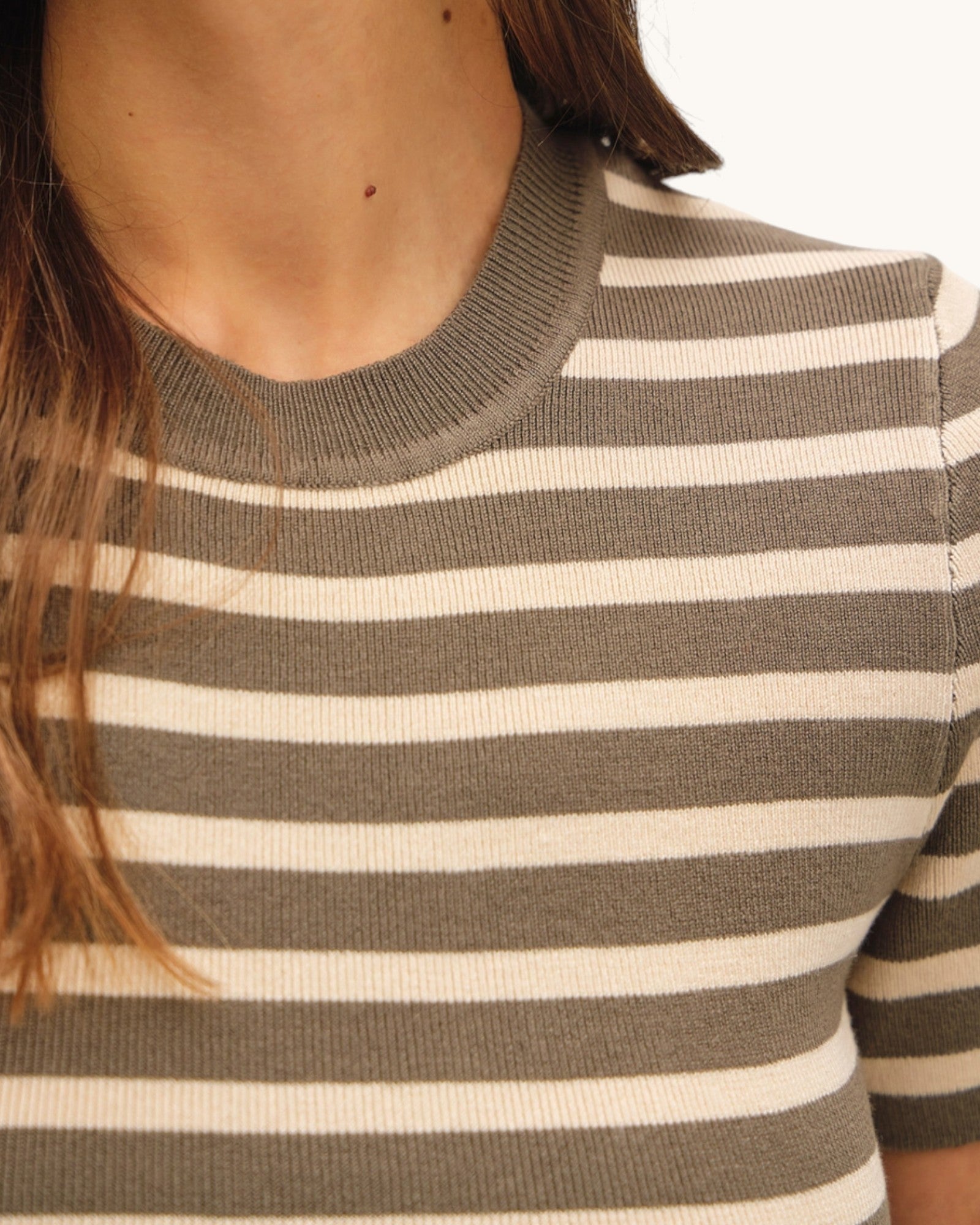 Close-up of a person wearing a olive/brown and ivory striped sweater top.
