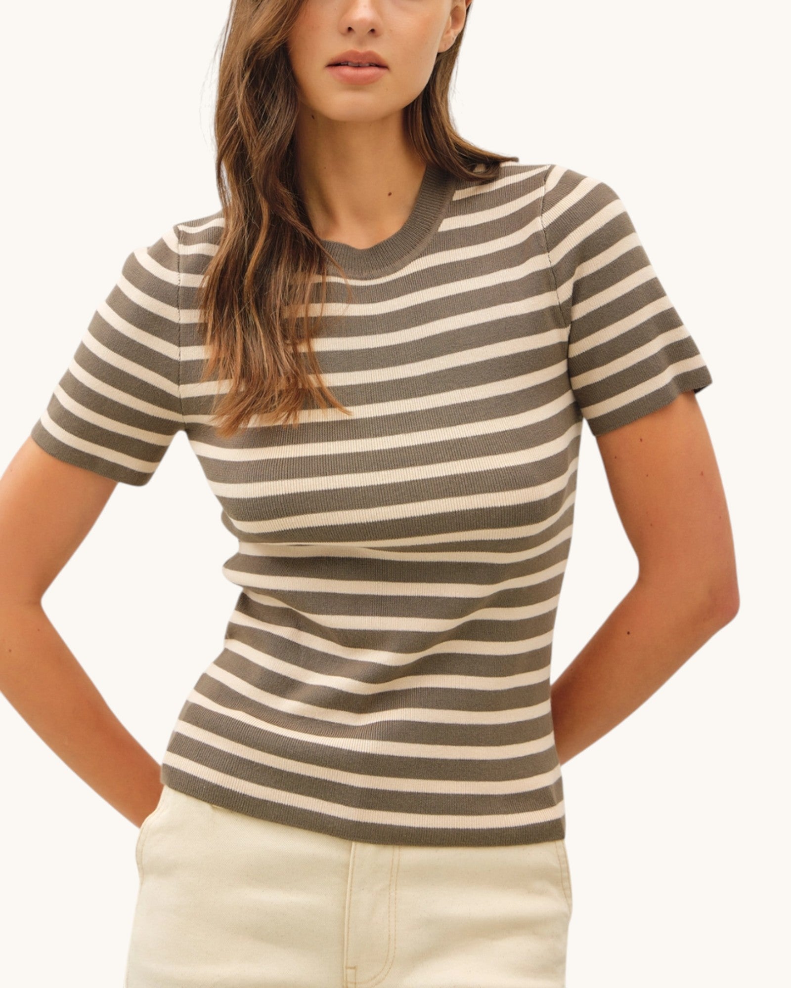 Woman wearing a striped olive lightweight sweater top with a plain background.
