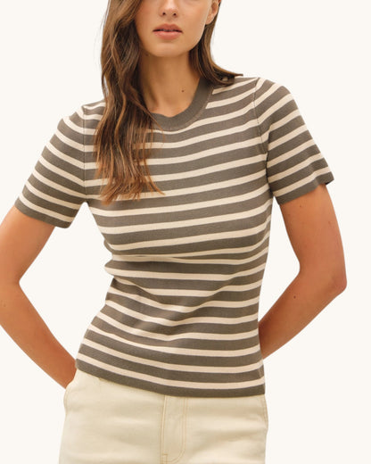 Woman wearing a striped olive lightweight sweater top with a plain background.