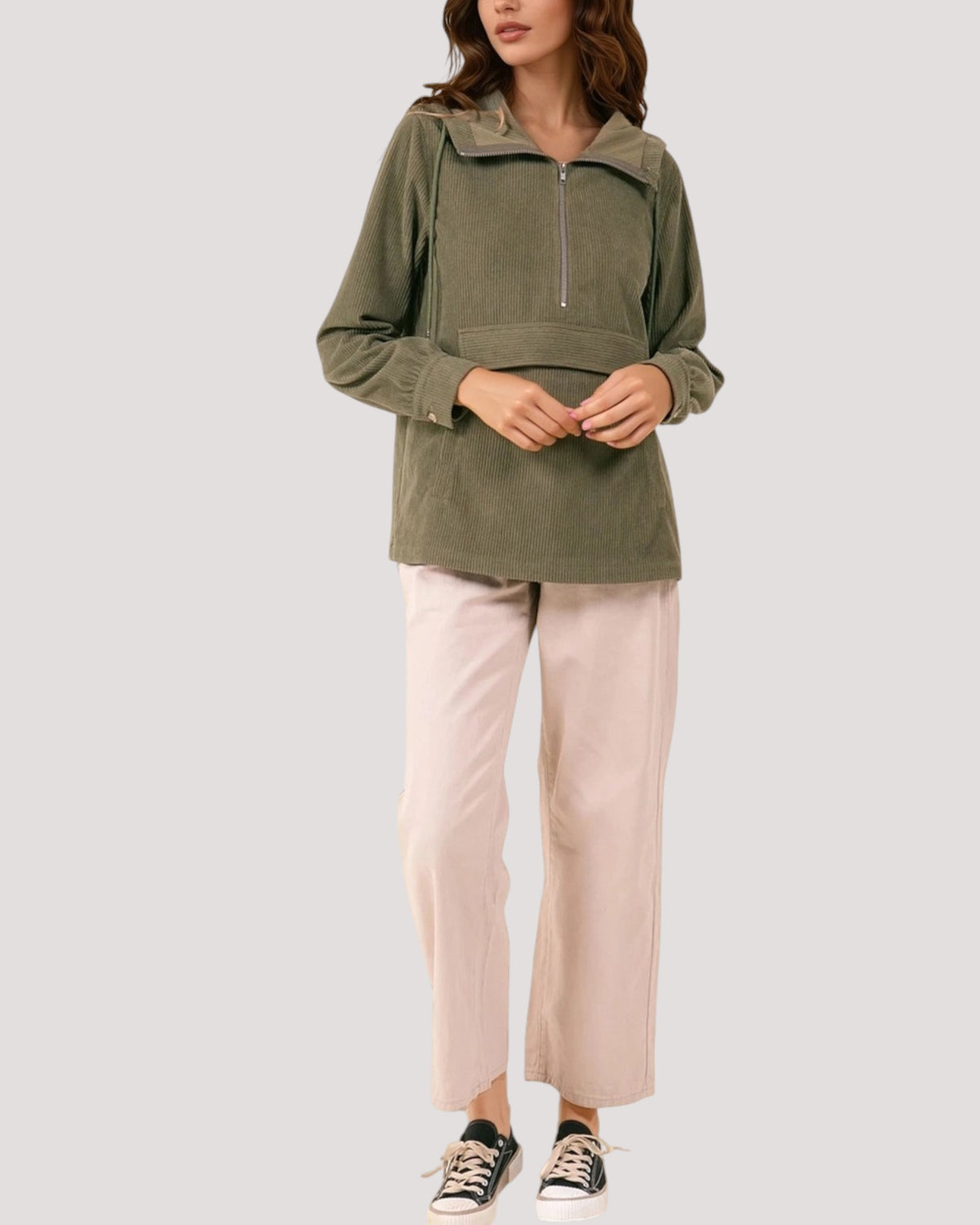 A woman models an olive green half-zip pullover jacket with a mock neck, paired with light pink wide-leg pants and black sneakers, against a solid light gray background.