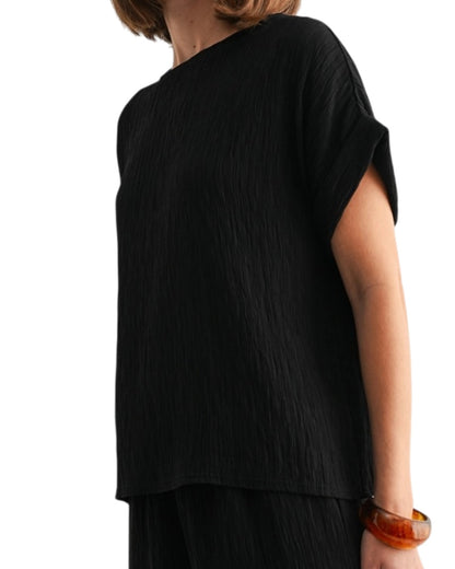 Black woven and textured short sleeve top worn by a person on a white background.