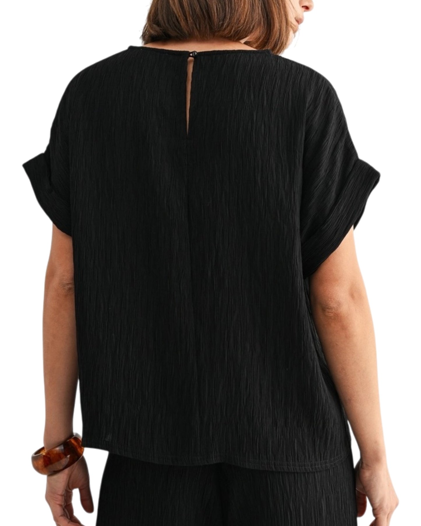 Black woven and textured short sleeve top worn by a person on a white background.
