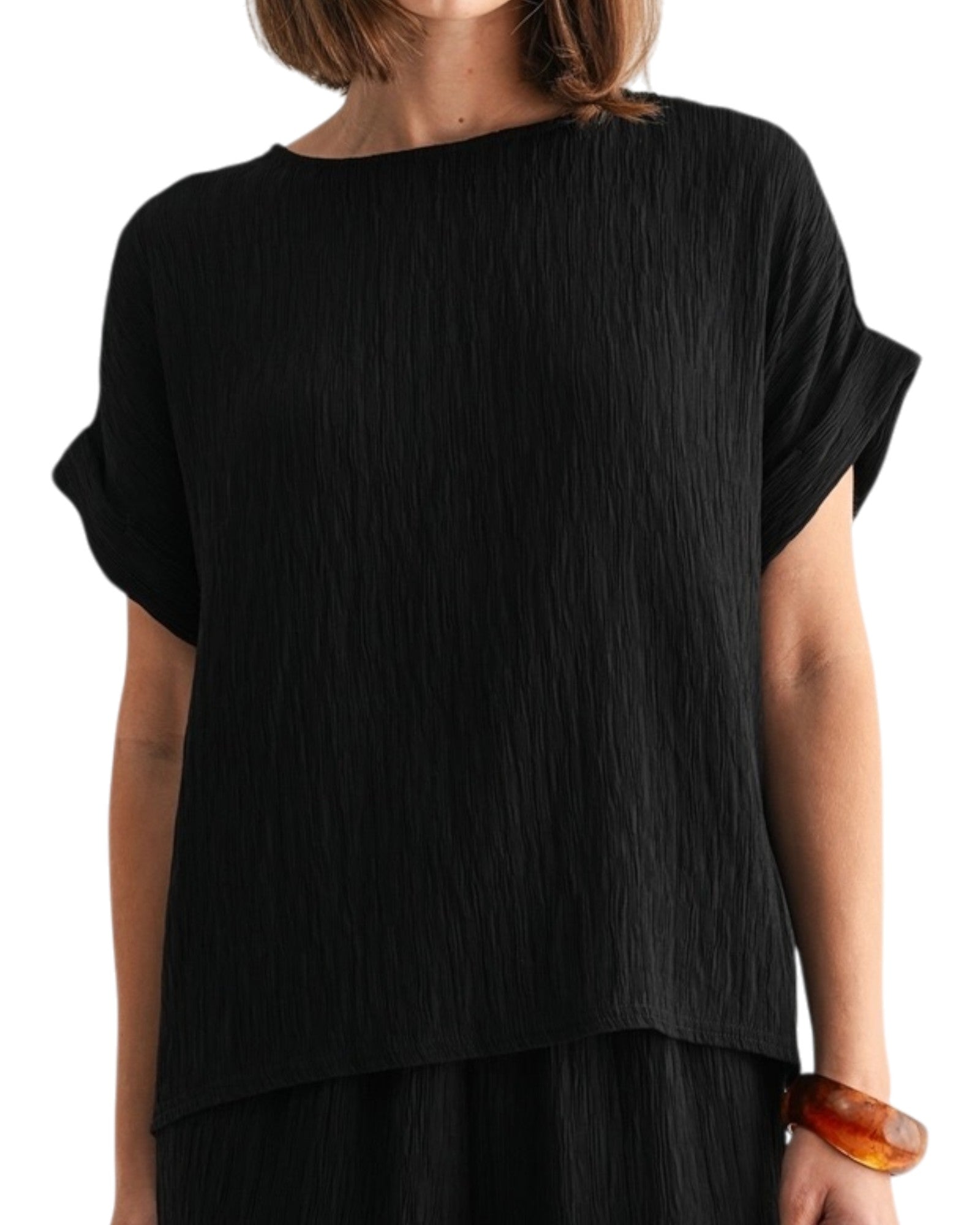 Black woven and textured short sleeve top worn by a person on a white background.