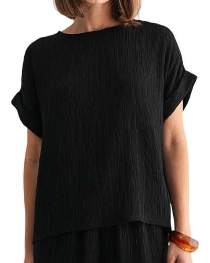 Black woven and textured short sleeve top worn by a person on a white background.