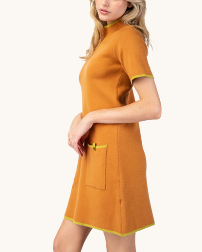 Side view of a model wearing a ginger short sleeve mock neck sweater dress with lime contrast trim and front patch pockets.