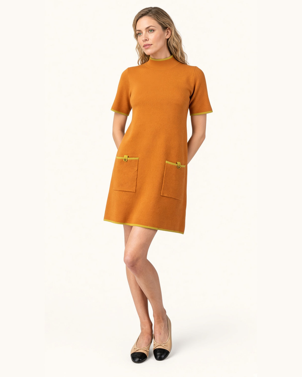 Model wearing a ginger short sleeve mock neck sweater dress with lime contrast trim and front patch pockets with tan and black ballet shoes.