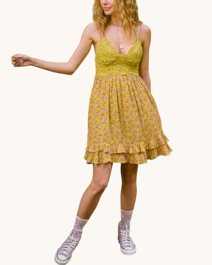 Woman wearing a olive floral dress with pink shoes on a white background.