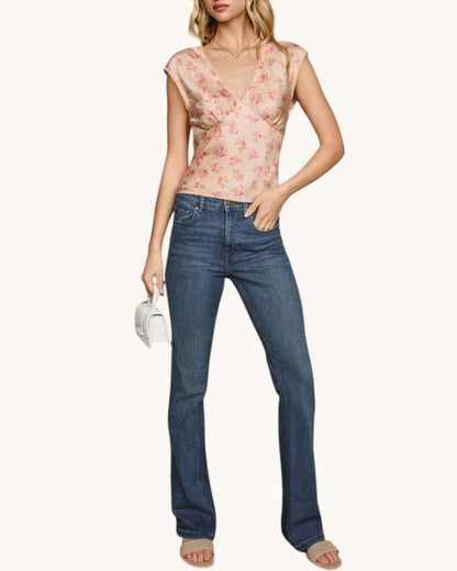 Woman wearing a floral top and blue jeans on a white background.