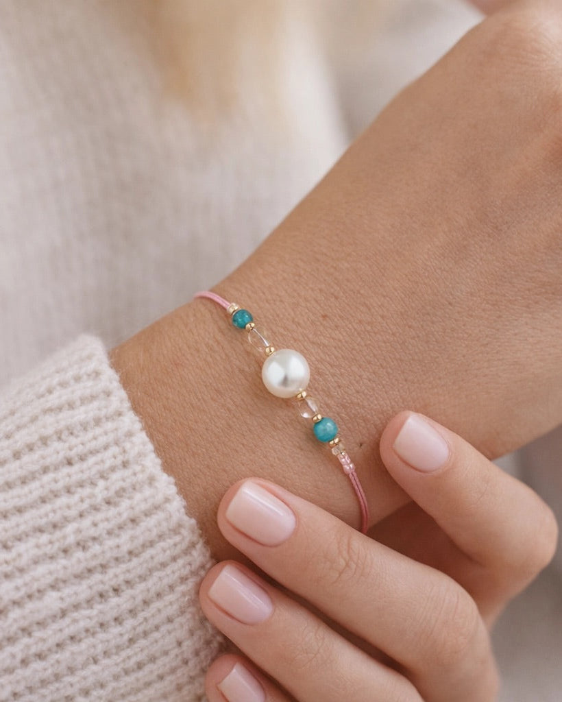 Close-up of a hand wearing a bracelet with a pearl and turquoise beads.