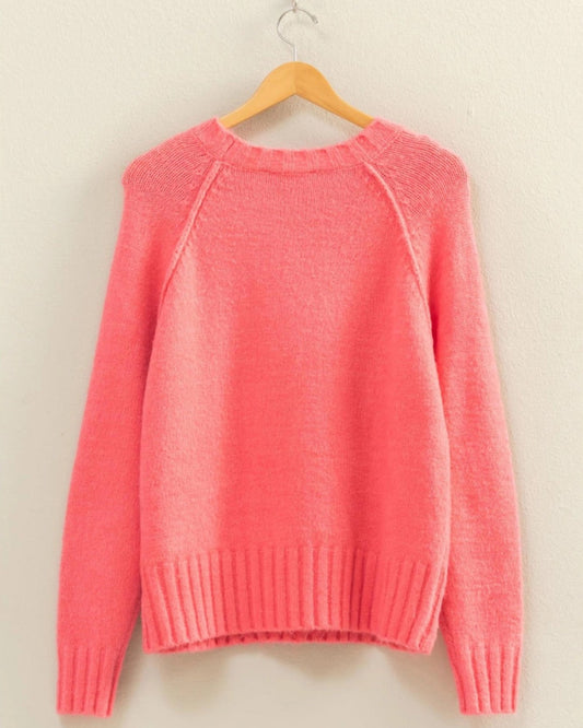 Pink sweater on a wooden hanger against a beige wall