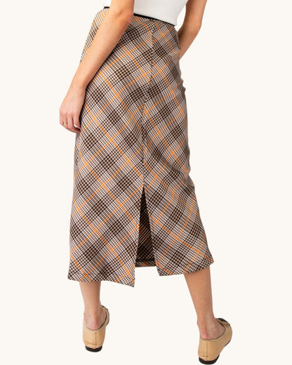 Back view of a brown, cream, and orange grid plaid midi pencil skirt with a middle slit. 