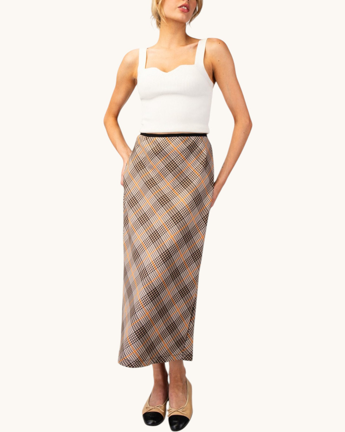 Model wearing a brown, cream, and orange grid plaid midi pencil skirt front view with a white tank top and nude/black ballet flats.