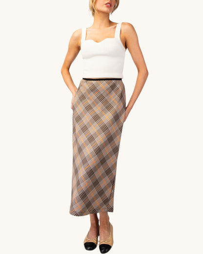 Model wearing a brown, cream, and orange grid plaid midi pencil skirt front view with a white tank top and nude/black ballet flats.
