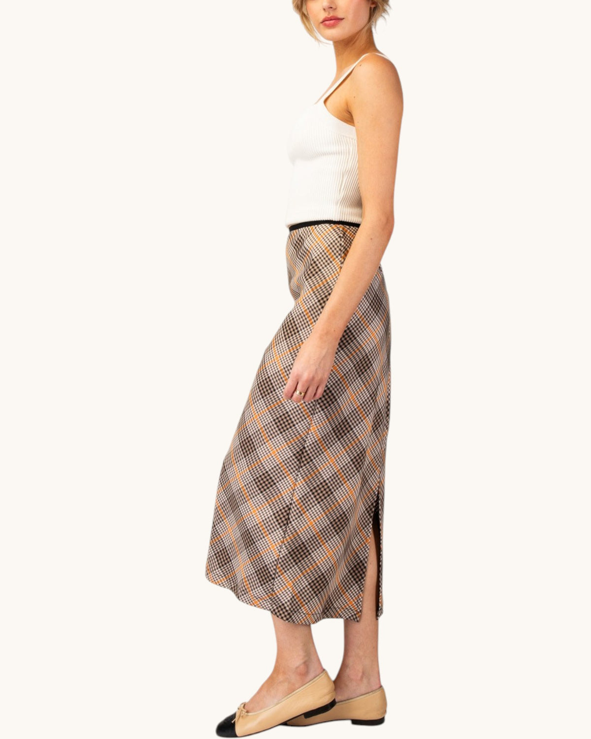 Side view of model wearing a brown, cream, and orange grid plaid midi pencil skirt front view with white tank top.