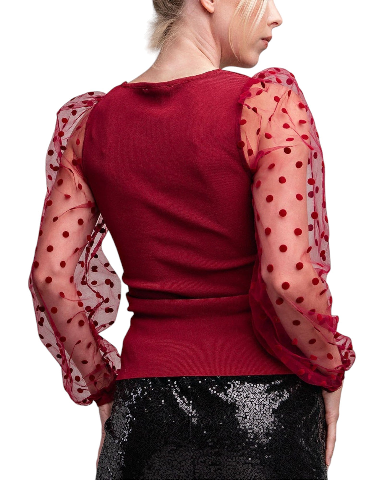 Woman wearing a merlot colored top with long, sheer sleeves with velvet polka dots. 