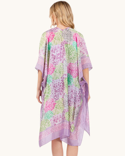 Back view of a woman wearing a colorful floral kimono-style garment in purple on a white background.