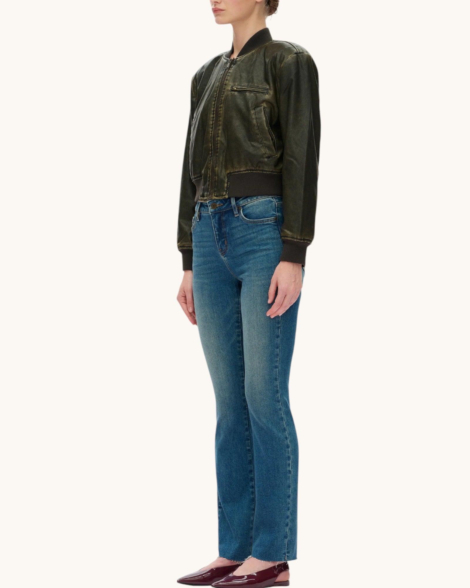 A model shown from the side wearing a dark olive green bomber jacket, blue jeans, and burgundy flats, set against a plain off-white background.