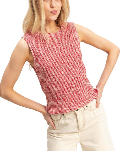 Woman wearing a red checkered sleeveless top and beige pants on a white background.