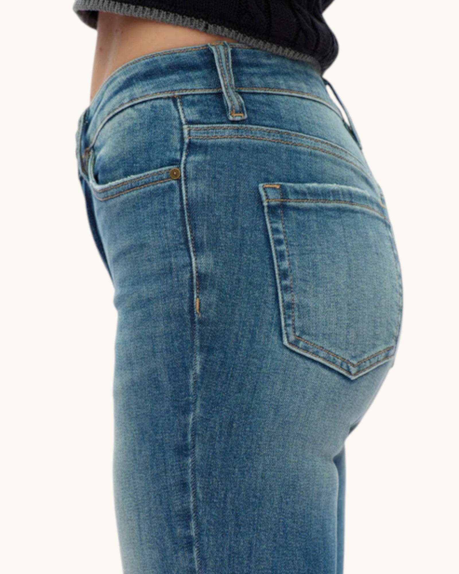 Close-up side view of a person wearing medium-wash blue denim jeans, showing the back pocket and waistband against a plain light background.