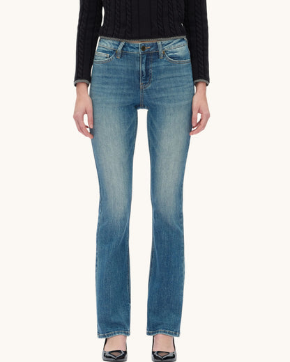 A model from the waist down wearing medium-wash blue denim bootcut jeans, a black cable-knit sweater, and black pointed-toe heels, set against a plain off-white background.