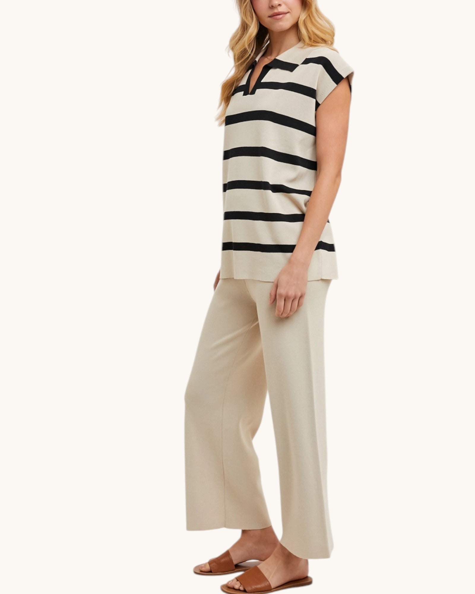 Woman wearing a black and beige striped top and beige pants on a white background.