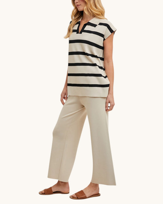 Woman wearing a black and beige striped top and beige pants on a white background.