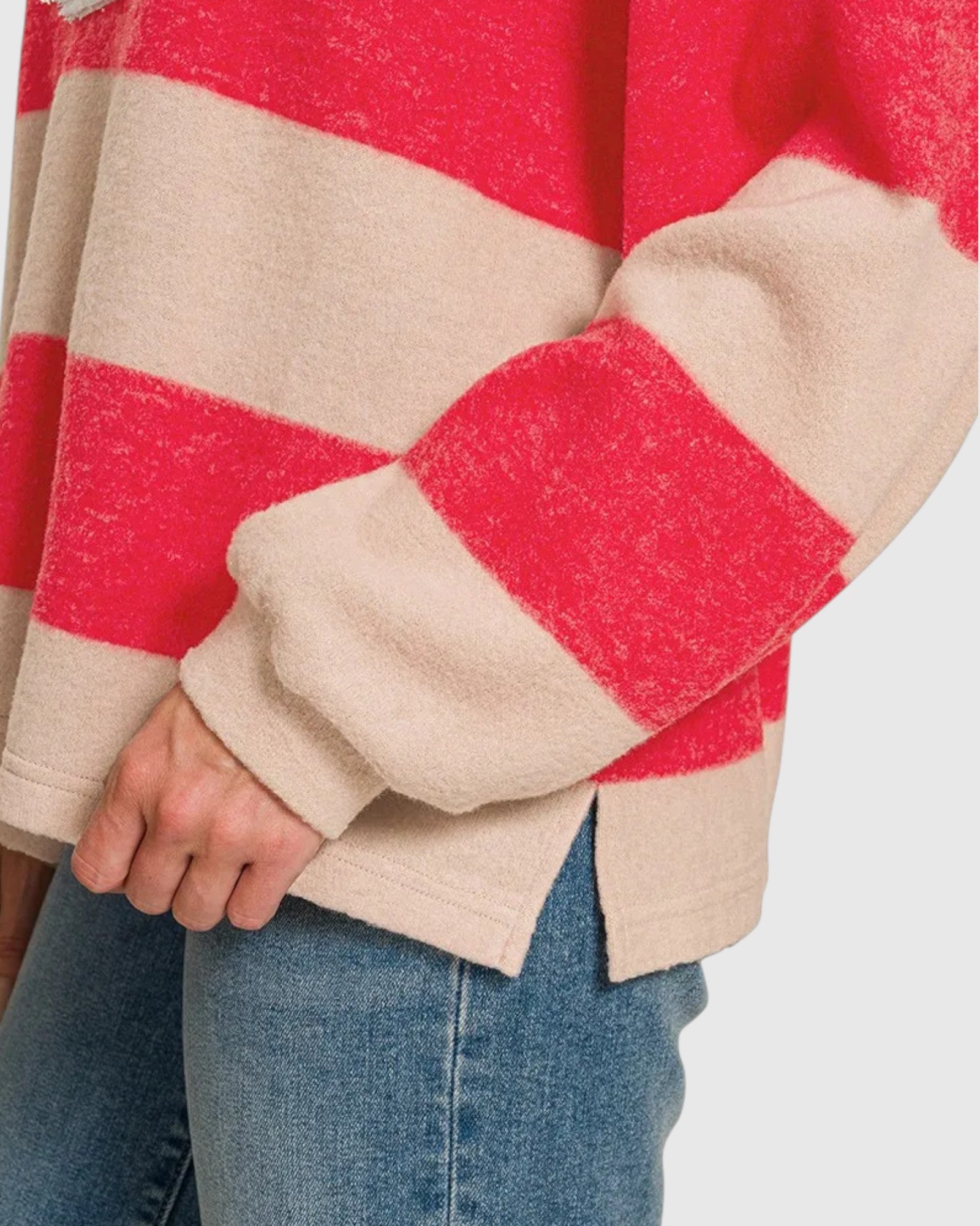A close-up of a person wearing a fuzzy knit sweater with bold horizontal red and beige stripes, paired with blue jeans.