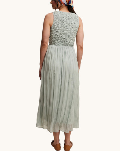 Woman wearing a light green textured top and pleated skirt set on a white background.