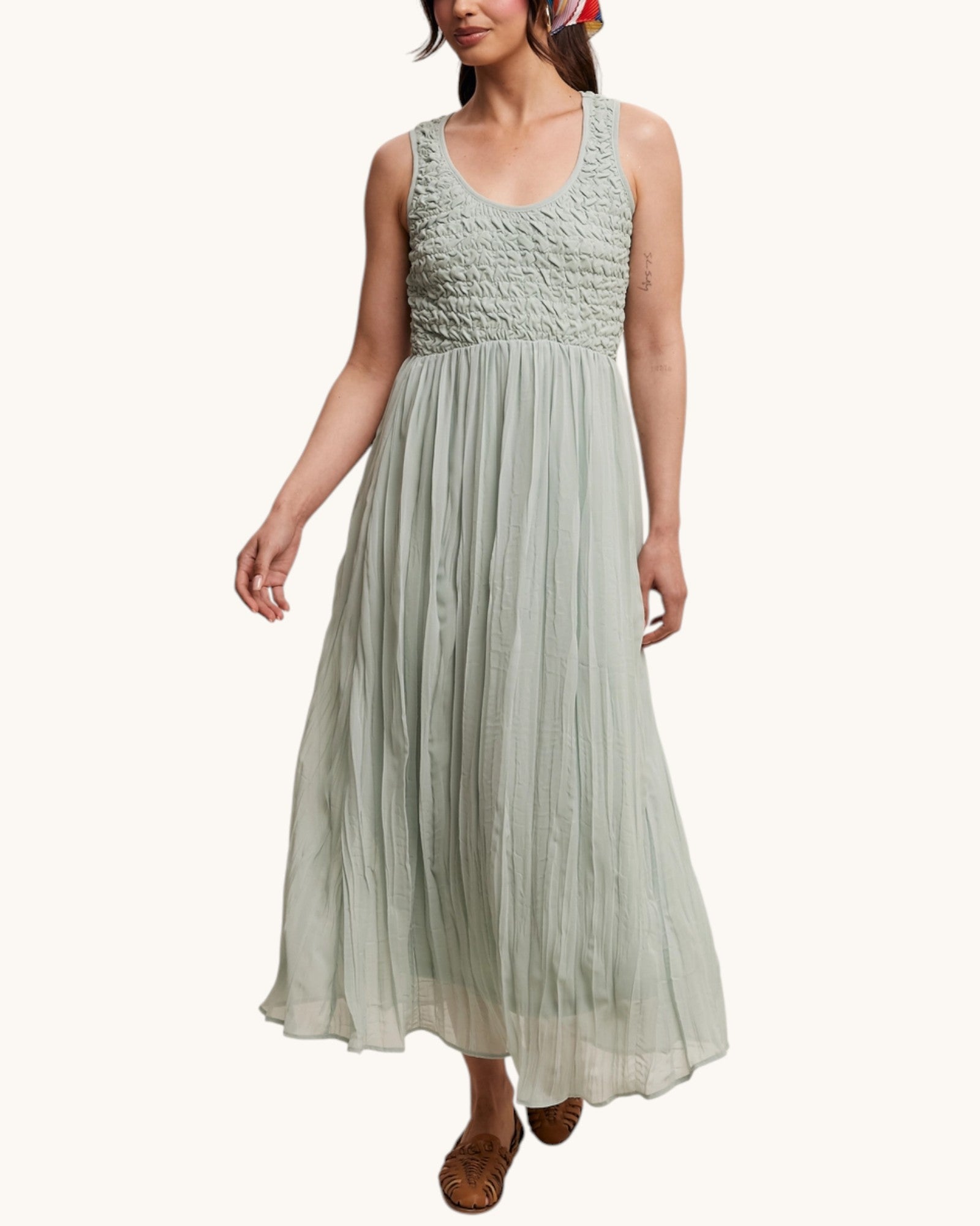 Woman wearing a light green dress with smocked bodice and flowing skirt on a white background.