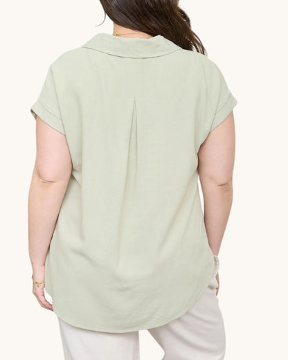 Person wearing a light green blouse with short sleeves on a white background, back view. 