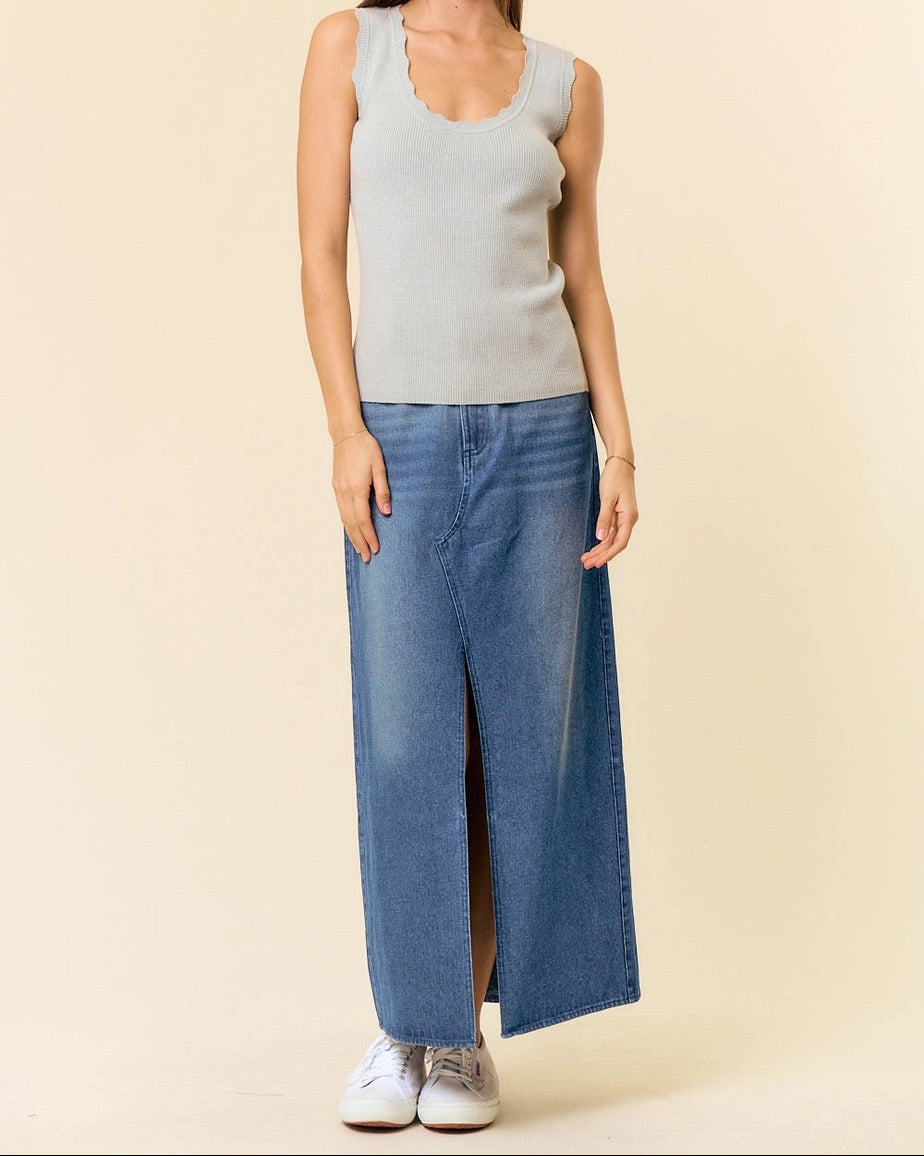 Woman wearing a light green scallop edge and ribbed sleeveless top and denim maxi skirt against a beige background.
