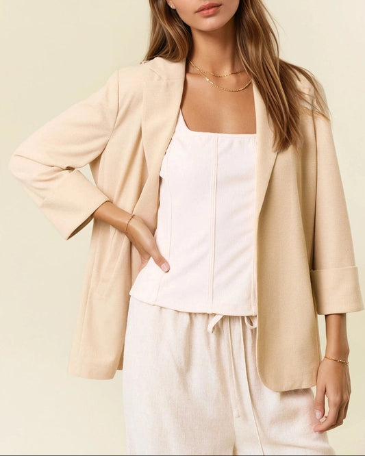 Woman wearing a beige blazer over a white top and pants on a light background.