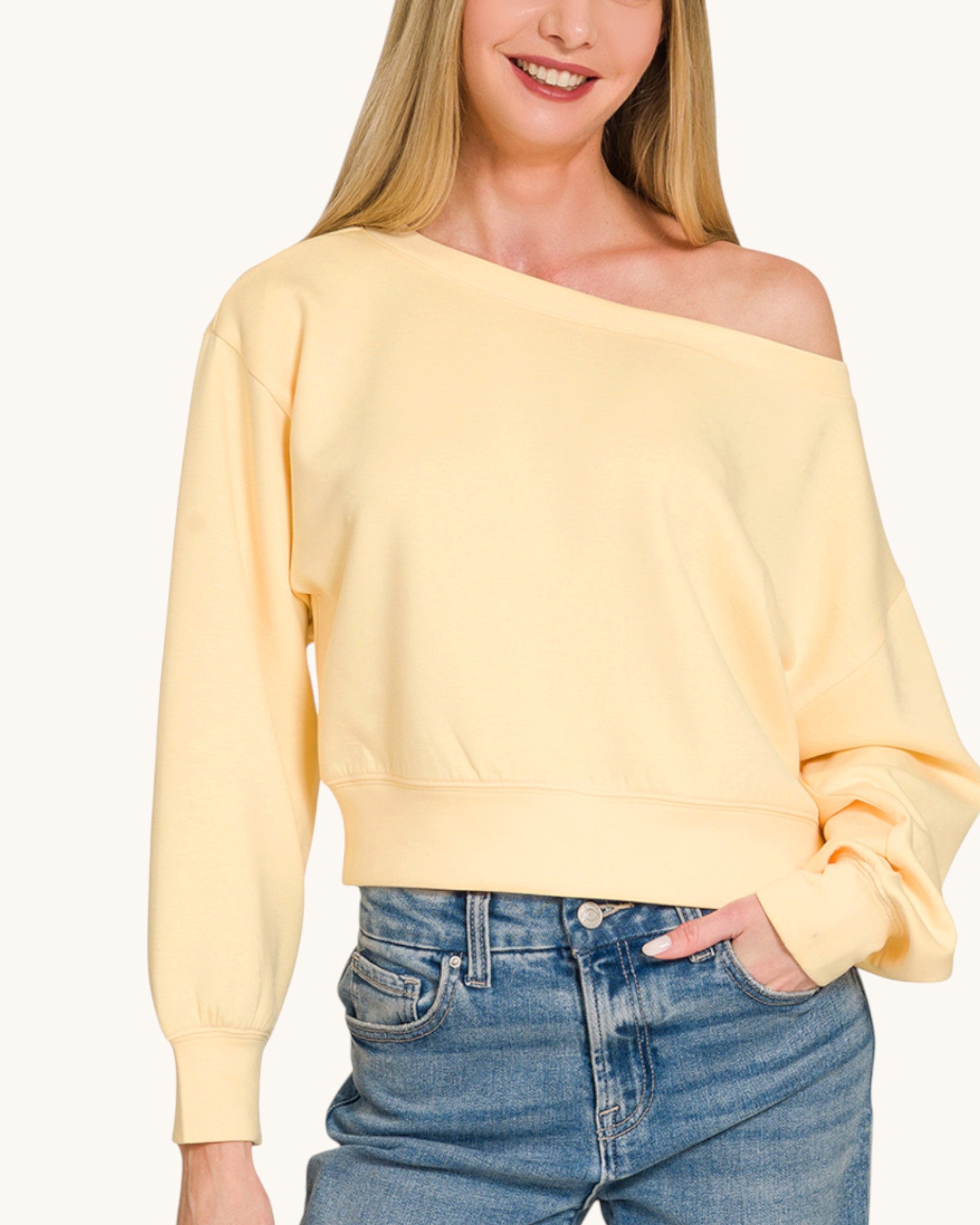 Woman wearing a yellow off-shoulder sweatshirt and blue jeans on a white background.