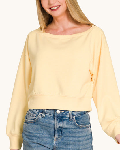 Woman wearing a yellow cropped sweatshirt and blue jeans on a white background.