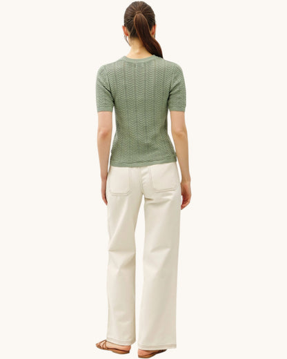 Back  view of a woman wearing a green patterned chevron short sleeve sweater and khaki pants on a white background.