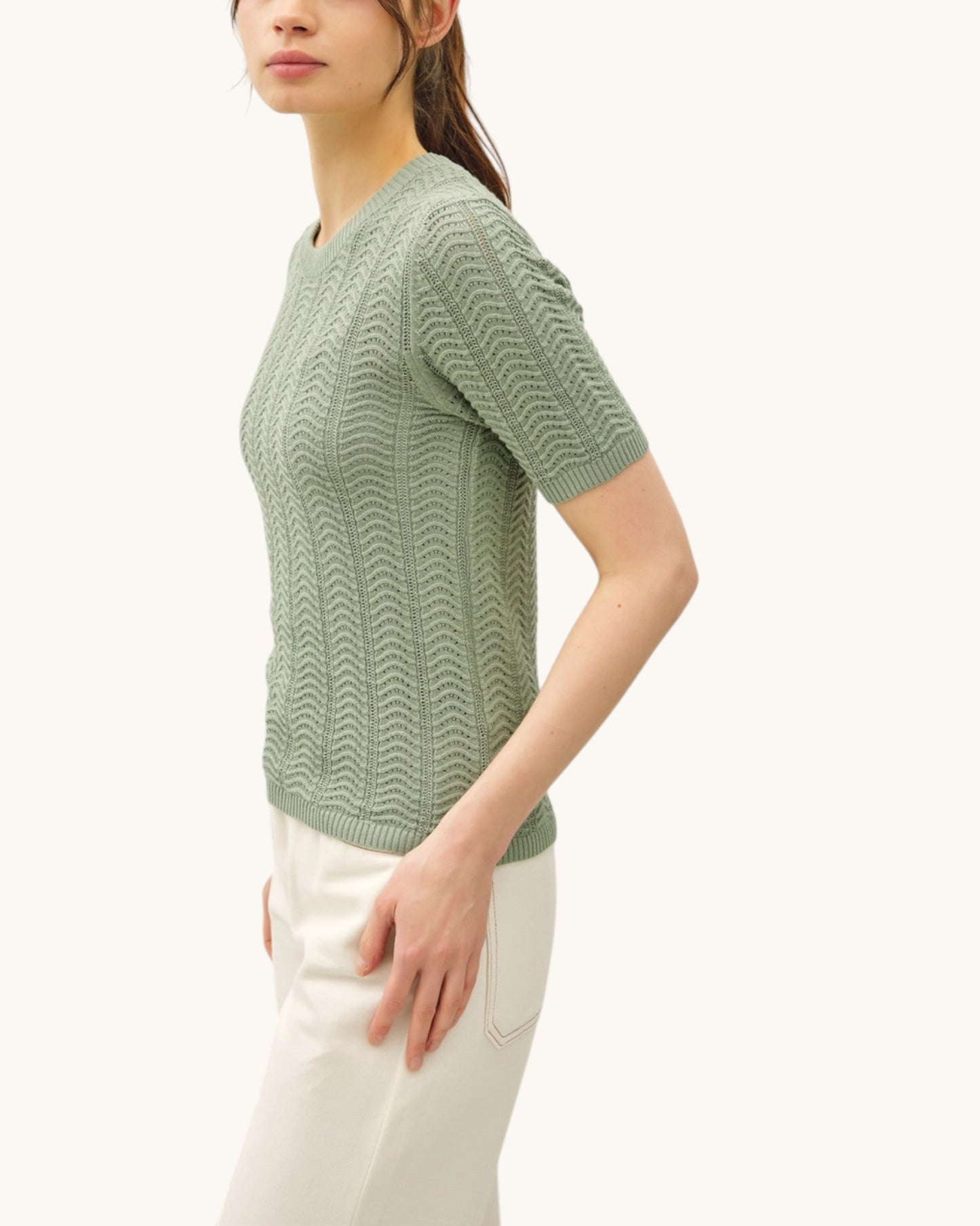 Side view of a woman wearing a green patterned chevron short sleeve sweater on a white background.