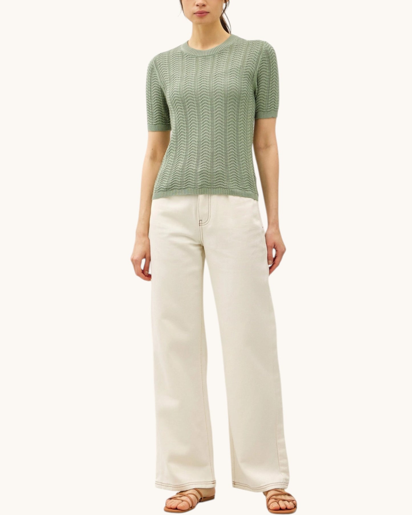 Woman wearing a green short sleeve sweater and white pants on a white background.