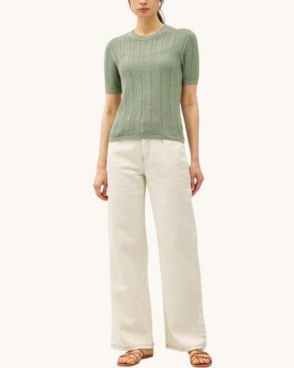 Woman wearing a green short sleeve sweater and white pants on a white background.