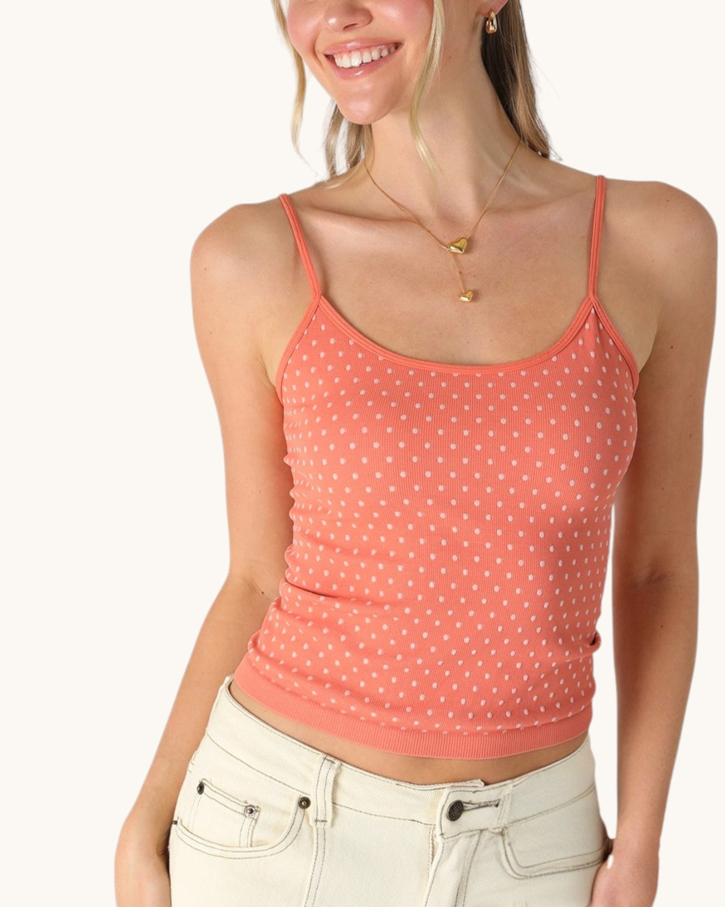 Woman wearing a coral polka dot tank top on a white background.