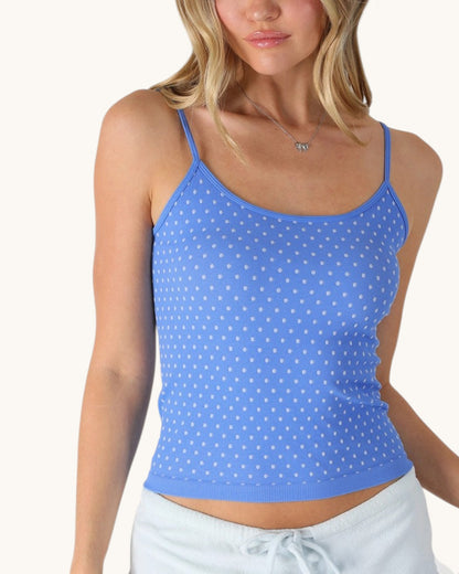 Woman wearing a blue polka dot tank top on a white background.