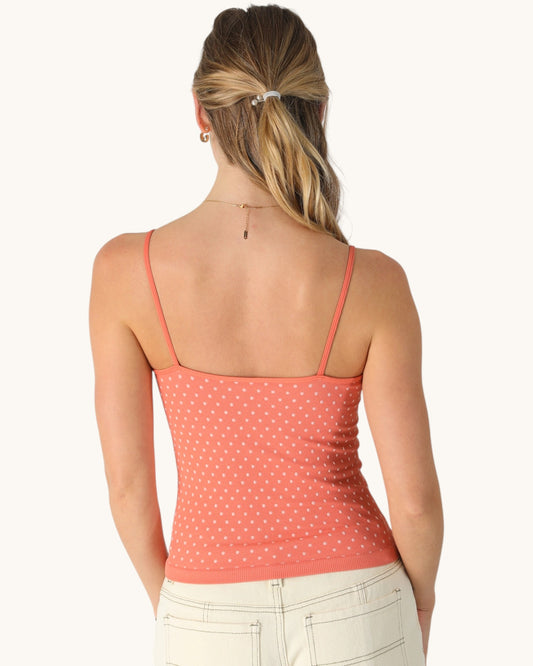 Back view of a woman wearing a coral polka dot tank top on a white background.