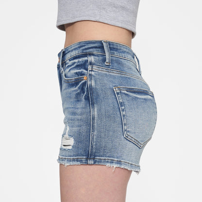 Woman wearing high-rise medium blue denim shorts with distressed details and a raw hem.