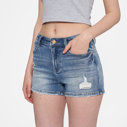 Woman wearing high-rise medium blue denim shorts with distressed details and a raw hem. 